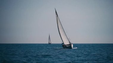 Bir yelkenli, yaz güneşinin altında güçlü rüzgarlarla mavi dalgaları aşarak özgürlük ve macera hissini yakalar..