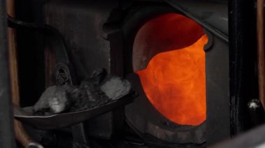 İtfaiyeci, yanan bir buhar trenine kömür atar. Yoğun alevler, tam faaliyet sırasında açık fırından görünür..