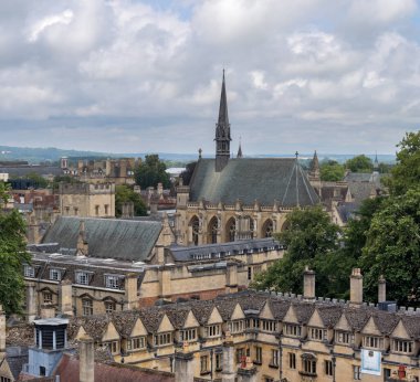 Tarihi bir üniversite kampüsünde antik binalar ve bulutlu gökyüzünün altında zamansız mimari güzelliğini vurgulayan büyük bir şapel yer alıyor..