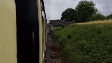 Eski bir kömür treni köprünün altından geçerken yoğun bir duman yayar, bir vagondan çekilir, yolculuğun ileri görüşlü görüntüsünü verir..