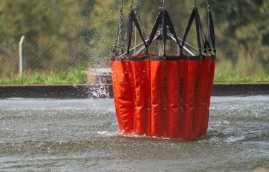 Bir Bambi Kovası havadan itfaiye için gölet suyuyla doludur. Bu da orman yangını yönetiminde önemli bir adımı gösterir..