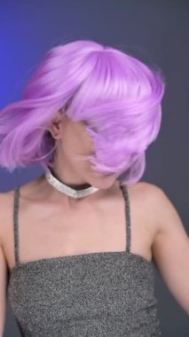 Mor peruklu muhteşem bir kız stüdyoda poz veriyor. Portre. Renkli bir geçmiş. Yavaş çekim, 120 fps, dikey