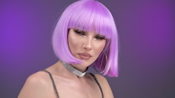 スタジオでは紫のウィッグの高級モデルがポーズをとっている 肖像画 紫色の背景 30Fps — ストック動画