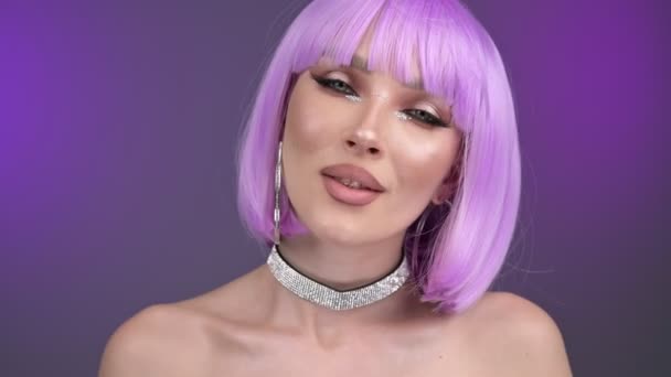 スタジオでは紫のウィッグの高級モデルがポーズをとっている 肖像画 紫色の背景 30Fps — ストック動画