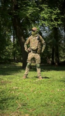 Savaş teçhizatı giyen bir asker yemyeşil bir arazide dimdik durur, hem hazırlık hem de iç gücünü gösterir.