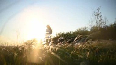 Huzurlu bir çayırda çarpıcı bir altın gün batımına karşı zarif bir şekilde poz veren bir kadının zarif silüeti.