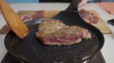 Sulu bir biftek, mükemmel yemek pişirmek için ahşap bir spatula kullanılarak dökme demir tavada ustalıkla çeviriliyor.