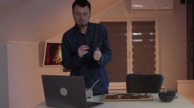 Modern bir adam, rahat bir çalışma ortamını tasvir eden şık ve rahat bir ev ofisinde dizüstü bilgisayarıyla tesadüfen etkileşime girer.
