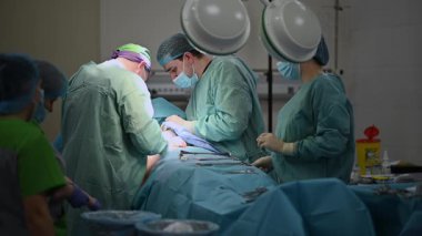Önlüklü yetenekli bir cerrahi ekibi parlak ve steril ışıklar altında detaylı bir operasyon yürütüyor.