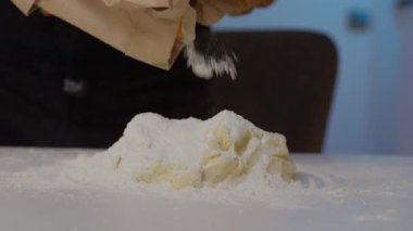 Bir insan sıcak ve rahat bir mutfakta lekesiz bir tezgahın üzerinde duran yuvarlak bir hamur topuna nazikçe un döker.
