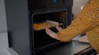 Büyüleyici ve rahat bir mutfağa, bir insan sıcak kurabiyelerle dolu bir tepsiyi şık bir fırına koyar.