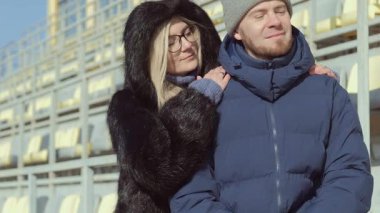 Bir çift, kış için sıcak kıyafetler giyerken boş bir stadyumda özel, samimi bir anın tadını çıkarıyor.