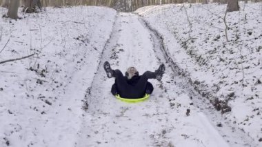Küçük bir çocuk neşeyle karlı bir tepeden kayıyor, ağaçların harikalar diyarına neşe içinde dalmış.