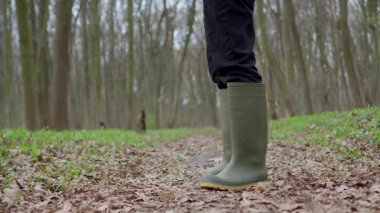 Parlak yeşil lastik çizmeler giyen bir insan, doğa tarafından sarılmış huzurlu ve huzurlu bir orman yolunda gezinir.