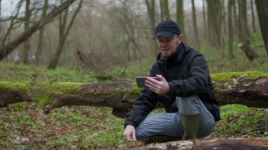 Bir insan akıllı telefonuyla sakin bir orman ortamında iletişim kurar, doğayla bağlantısını vurgular..
