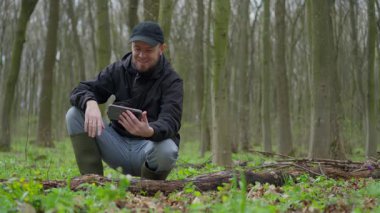 Huzurlu bir ormanda, doğanın güzelliğinin tadını çıkarırken tabletle etkileşime geçen bir adam.