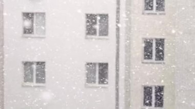 Güzel kar taneleri, durgun kış manzarasında beyaz binaların üzerine yavaşça düşüyor.