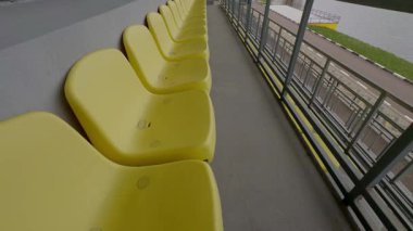 Modern bir stadyumda, atletizm pistine bakan bir dizi boş sarı koltuk.