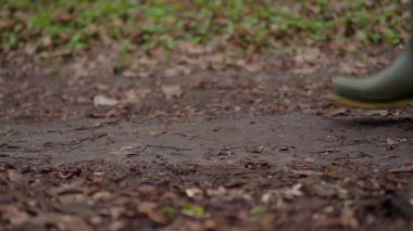 Bu canlı yeşil lastik botların, bereketli doğayla çevrili çamurlu zeminde adımlarını attığı yakın çekim görüntüsü.