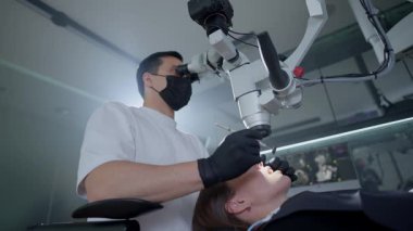 Modern diş kliniğinde ameliyat sırasında diş mikroskobu kullanan erkek dişçi ve asistan hastaların yakın çekimleri. Endodontist, kanal tedavisi asistanı. Diş hekimliğinde mikroskop kullanmak. Yüksek kalite 4k görüntü