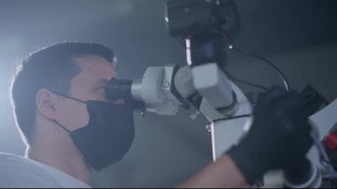 Odaklanmış bir tıp uzmanı, sağlık araştırmalarını vurgulayarak, bir örneği mikroskopla inceler..