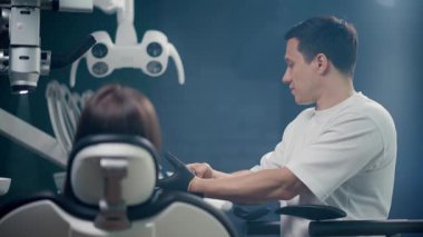 Bir dişçi, modern, çağdaş diş muayenehanesi ortamında bir hastaya profesyonel danışmanlık hizmeti sunar.