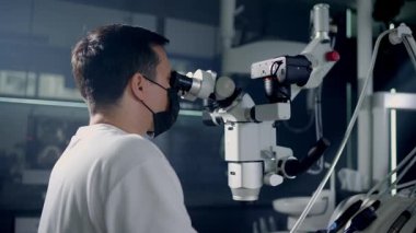 Odaklanmış bir cerrah, bir mikroskop kullanır, ileri tıbbi teknolojiyi klinik ortamda sergiler..