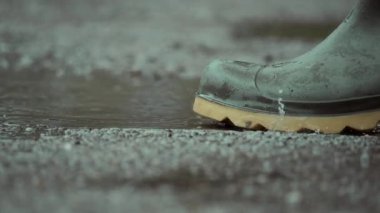 Bu resim, yağmur birikintilerinin arasından süzülen su geçirmez botların yakın çekimini gösteriyor, dinamik su hareketini vurguluyor.