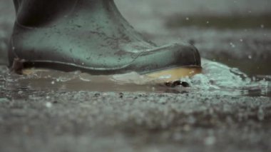 Yağmurlu bir günde su birikintilerine sıçrayan şık botların yakın çekimi heyecan verici sıçramaları ve yansımaları vurguluyor.
