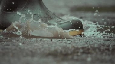 Yağmurlu bir günde su birikintilerine sıçrayan şık botların yakın çekimi heyecan verici sıçramaları ve yansımaları vurguluyor.