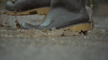 Siyah lastik botlar su birikintisine basar ve etrafta uçuşan bir sıçrama yaratır. Yavaş çekim, yüksek hız kamerası, 250 fps. Yüksek kaliteli FullHD görüntüler