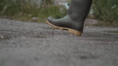 Neşeli bir insan neşeyle renkli lastik çizmelerle su birikintilerine sıçrıyor, yağmurun keyfini kutluyor.