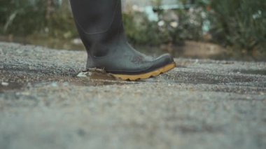 Neşeli bir insan neşeyle su birikintilerine sıçrar renkli lastik çizmeler giyer, yağmurlu günlerin eğlencesini kutlar.