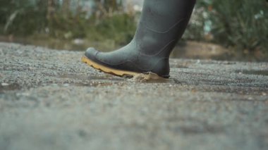 Su birikintilerine basan lastik botların yakın plan görüntüsü, sıçramalar yaratır ve doğanın özünü yakalar..