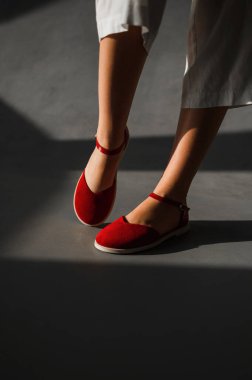 Şık kırmızı ayakkabılar giymiş bir kadın canlı ayakkabı seçimiyle çelişen pürüzsüz beton zeminde güvenle duruyor.