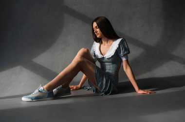 Zarif bir şekilde giyinmiş bir kadın rahat bir şekilde yerde oturur ve bacaklarını kavuşturur.