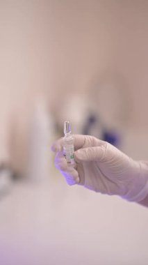 Eldivenli bir el, temiz ve steril bir laboratuvar ortamında şeffaf bir tıbbi şişeyi dikkatlice tutar.