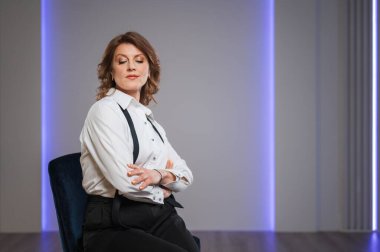 Kendine güvenen bir iş kadını zarif bir şekilde koltuğunda oturur ve modern bir ofiste profesyonelliğini gösterir.