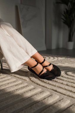 Bir kadın rahat bir şekilde rahat bir kanepede otururken şık siyah ayakkabılar giyiyor, genel görünüşüne ve titreşimlerine zarafet katıyor.