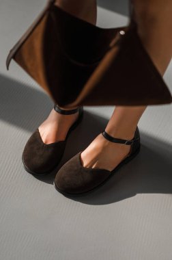 Bir kadın, elbisesini tamamlayan kahverengi bir çanta tutarken şık bir çift kahverengi ayakkabı giyerken görülebilir.