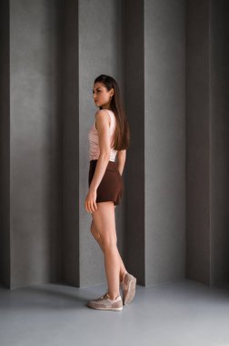 Kahverengi şortla birlikte şık pembe bir bluz giyen bir kadın rahatlamış tavrını sergiliyor.