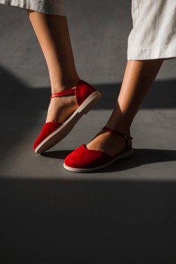 Şık kırmızı ayakkabılar giymiş bir kadın canlı ayakkabı seçimiyle çelişen pürüzsüz beton zeminde güvenle duruyor.