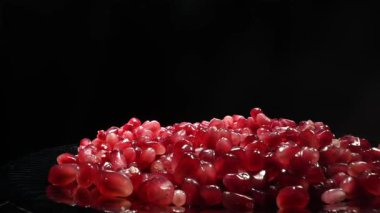 Canlı nar tohumları, koyu siyah bir zemin üzerinde güzel bir şekilde parlıyor, zarif zengin renklerini sergiliyorlar.