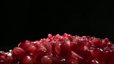 Canlı nar tohumları, koyu siyah bir zemin üzerinde güzel bir şekilde parlıyor, zarif zengin renklerini sergiliyorlar.