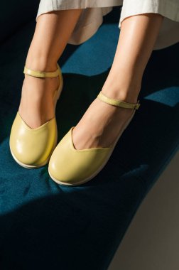 Şık bir çift parlak sarı ayakkabı giyen bir kadın rahat bir şekilde rahat bir odada, yumuşak mavi bir koltukta oturuyor.