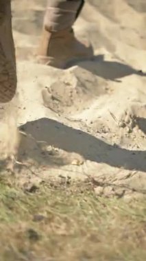 Bir asker kasten yukarıdaki açık mavi gökyüzünün altındaki geniş kumlu arazide yürür.