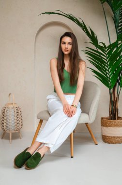 Zarif beyaz pantolonlu, çarpıcı yeşil bir mahsul giymiş bir kadın şık bir sandalyede rahatça oturabilir.