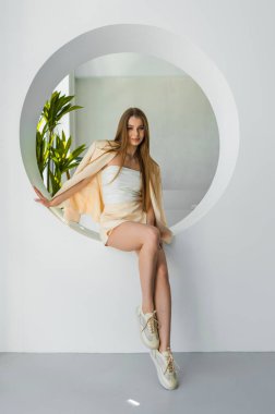 Şık bir model, spor ayakkabıları ve pastel tonlarıyla şık ve modaya uygun bir görünümü somutlaştıran, modern minimalist bir alanda kendine güvenen bir şekilde poz verir..