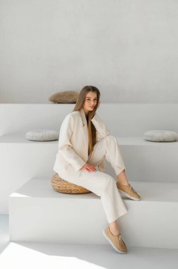 Bir model şık bej bir kıyafet sergiliyor, minimalist bir yüzeyde zarifçe oturuyor. Modern moda çekimleri için mükemmel..