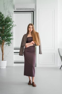 Şık bir kadın zarif bir şekilde modern bir yaşam alanında yürüyor, şık kıyafetlerini ve uzun saçlarını sergiliyor..